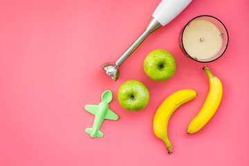 Homemade baby food. Cook puree with apple and banana with immersion blender. Pink background with toy top view space for text