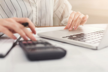 Closeup of woman hands counting on calculator and typing on laptop