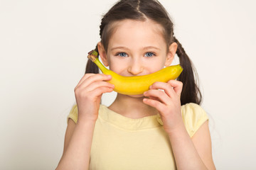 Happy little girl having fun with banana over white background