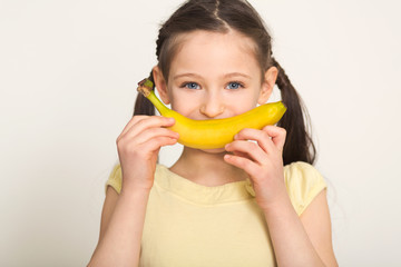 Happy little girl having fun with banana over white background © Prostock-studio