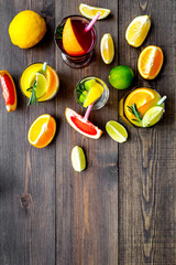 Tropical fruit cocktail with alcohol. Glass with beverage near oranges, grapefruit, lime and rosemary on dark wooden background top view space for text