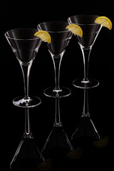 Three martini glasses on ablack reflective surface, each with a slice of lemon