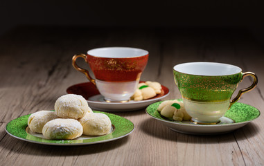 One green and one red tea cup and saucer with a plate of cookies