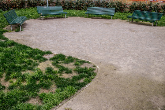 Panchine verdi a doghe in semicerchio in uno spiazzo di terra battuta  di un parco pubblico