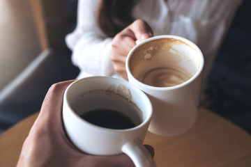Close up image of a man and a woman clinking white coffee mugs in cafe