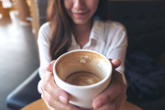 Closeup image of an Asian woman holding and showing a cup of coffee before drink it with feeling good in cafe