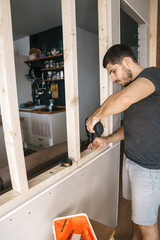 Male with a Screwdriver in his hand fixes a wooden structure for a window in his house. Repair yourself.