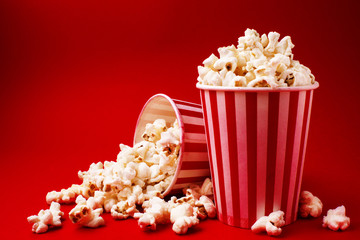 popcorn in a striped box, next inverted box with popcorn, on a red background, side view