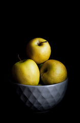 Bowl of yellow apples. On black background.