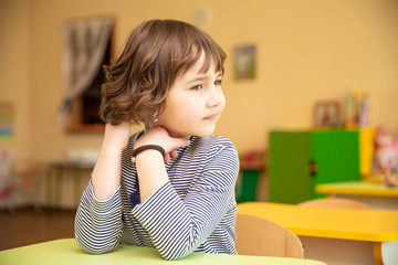 Portrait of cute little girl sitting with hands clasped at desk in classroom