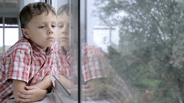 sad little boy standing near a window at home  at the day time