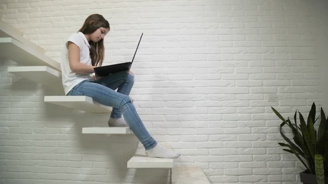 online internet pastime. young teen seeting on stairs and browsing laptop entertainment resources.