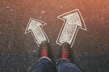 Sneakers on the asphalt road with drawn arrows pointing in two directions. Making decisions and...