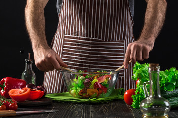 Man preparing salad with fresh vegetables on a wooden table. Cooking tasty and healthy food
