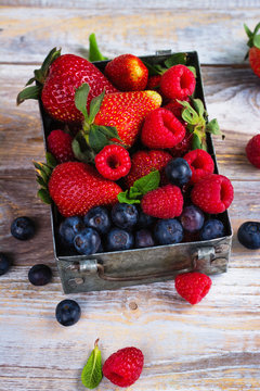 Fresh mix of berries in a metal box on white stone background