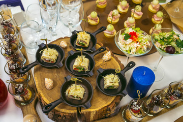 Beautiful decorated catering banquet table with different food snacks and appetizers. Canape rolls in small pans on wood