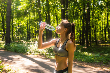 Young woman drinking water after jogging outdoors