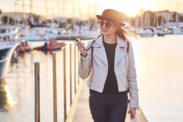 Pretty young woman in black hat with vape at a sea port