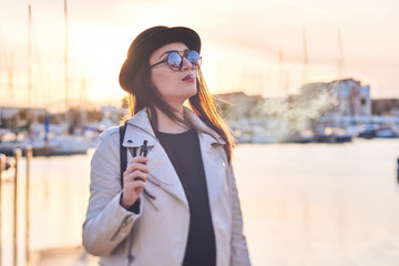 Fototapeta premium Pretty young woman in black hat with vape at a sea port