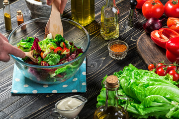 Man preparing salad with fresh vegetables on a wooden table. Cooking tasty and healthy food. Close-up