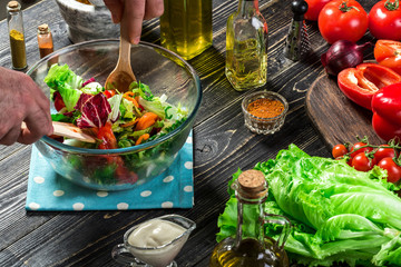 Man preparing salad with fresh vegetables on a wooden table. Cooking tasty and healthy food. Close-up