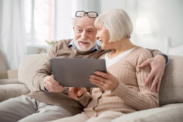 Modern entertainment. Delighted aged couple looking at the tablet screen while having fun together