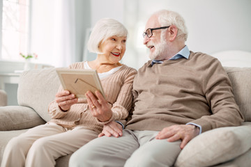 Our memories. Nice pleasant elderly woman holding a photograph while sitting together with her husband