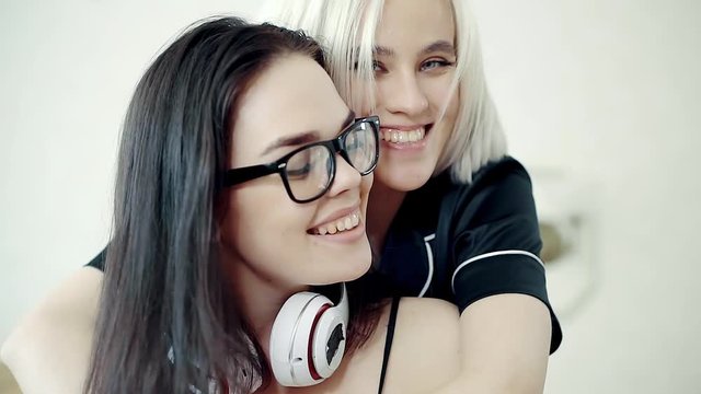 Cheerful girl is placing earphones on neck of brunette woman and embracing her from back. Girl is surprising and smiling calmly in her grabs