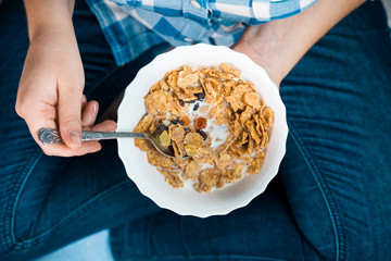 Girl with a plate of cereal. Flakes from whole wheat with dried fruits. Healthy eating concept. A girl in jeans and a plaid shirt. Proper nutrition. Healthy food.