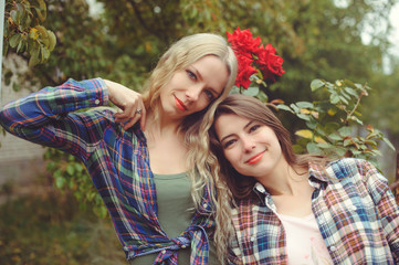 cheerful attractive two young blonde girl and brunette posing against nature background, wearing jeans and shirts, sisters