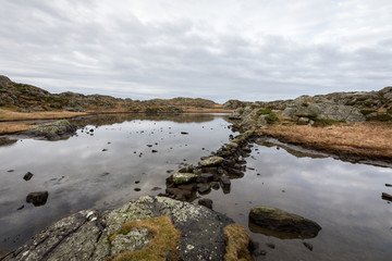 Fototapeta na wymiar Pond by the trail, at the Rovaer archipelago, island in Haugesund, Norway. Stones making a path through the water.