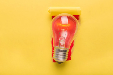 Light bulb at torn yellow paper background