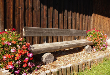 Holzbank am Wegesrand mit Blumenschmuck