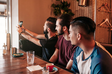 Group of arab friends taking selfie in lounge bar. Mixed race young men having fun. Best friends hangout together