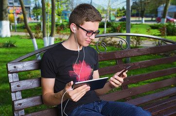 Obraz premium A young guy in the Park uses gadgets, smartphone and tablet