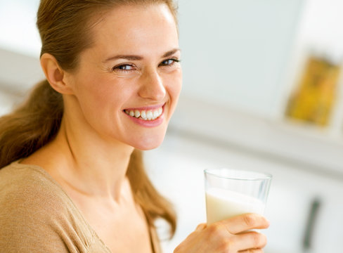 smiling young woman with glass of milk in kitchen