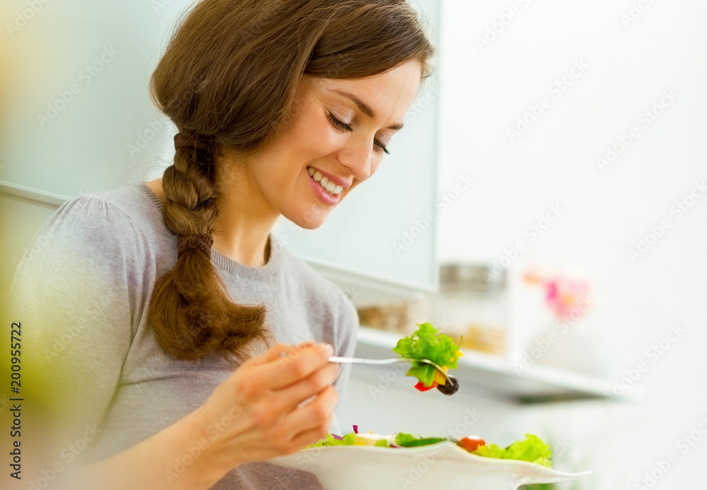 Wall mural Young woman eating fresh salad in modern kitchen