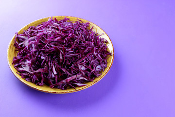 Chopped cabbage on a violet background, red cabbage on a yellow plate, copy space, top view, vegetarian food, fresh vegetables for salad, ultraviolet background, minimalism