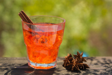 a glass with an exotic red carbonated drink with ice, a cinnamon stick in the glass, the badyan stars lie in a glass