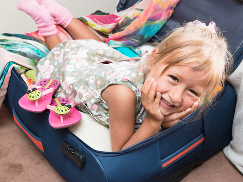 A small tanned cute little girl traveler gathers a suitcase. She indulges and helps her mother to pack things carefully. Tourist attribute. Order in suitcase. Cild. Kid.