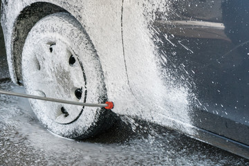 Car washing process of luxury car full covered with white foam and splashes from water gun