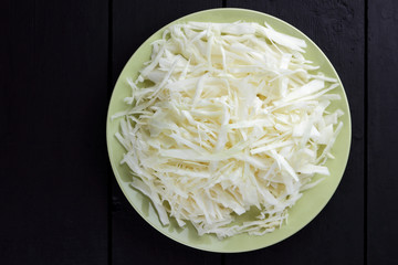 Chopped cabbage on a black background, white cabbage on a green plate, copy space, top view, vegetarian food, fresh vegetables on dark boards, black background, minimalism