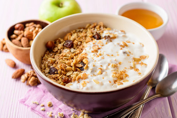 Granola with yogurt in bowl on pink wooden background.