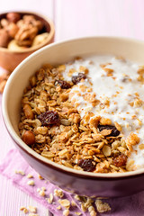 Granola with yogurt in bowl on pink wooden background.