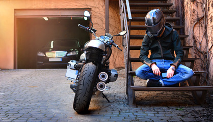 Lonely biker thought about and rested on the stairs near the motorcycle. Motorbike and motorcyclist...