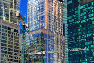 Construction cranes on the background of glass facades of skyscrapers in sunny day