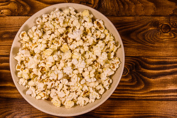 Ceramic plate with popcorn on wooden table. Top view
