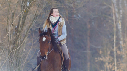 Young female rider riding a black horse through the drifts in the winter frozen forest