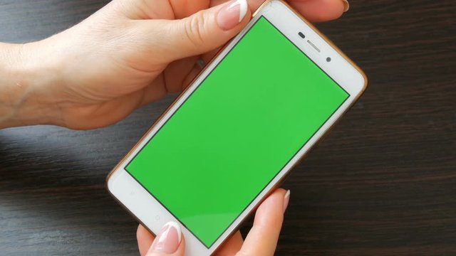 Female hands with beautiful French manicure take a white smartphone with Green Screen. Using Smartphone,Holding Smartphone with Green Screen