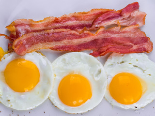Fried egg with bacon on white plate. Delicious colorful English breakfast.